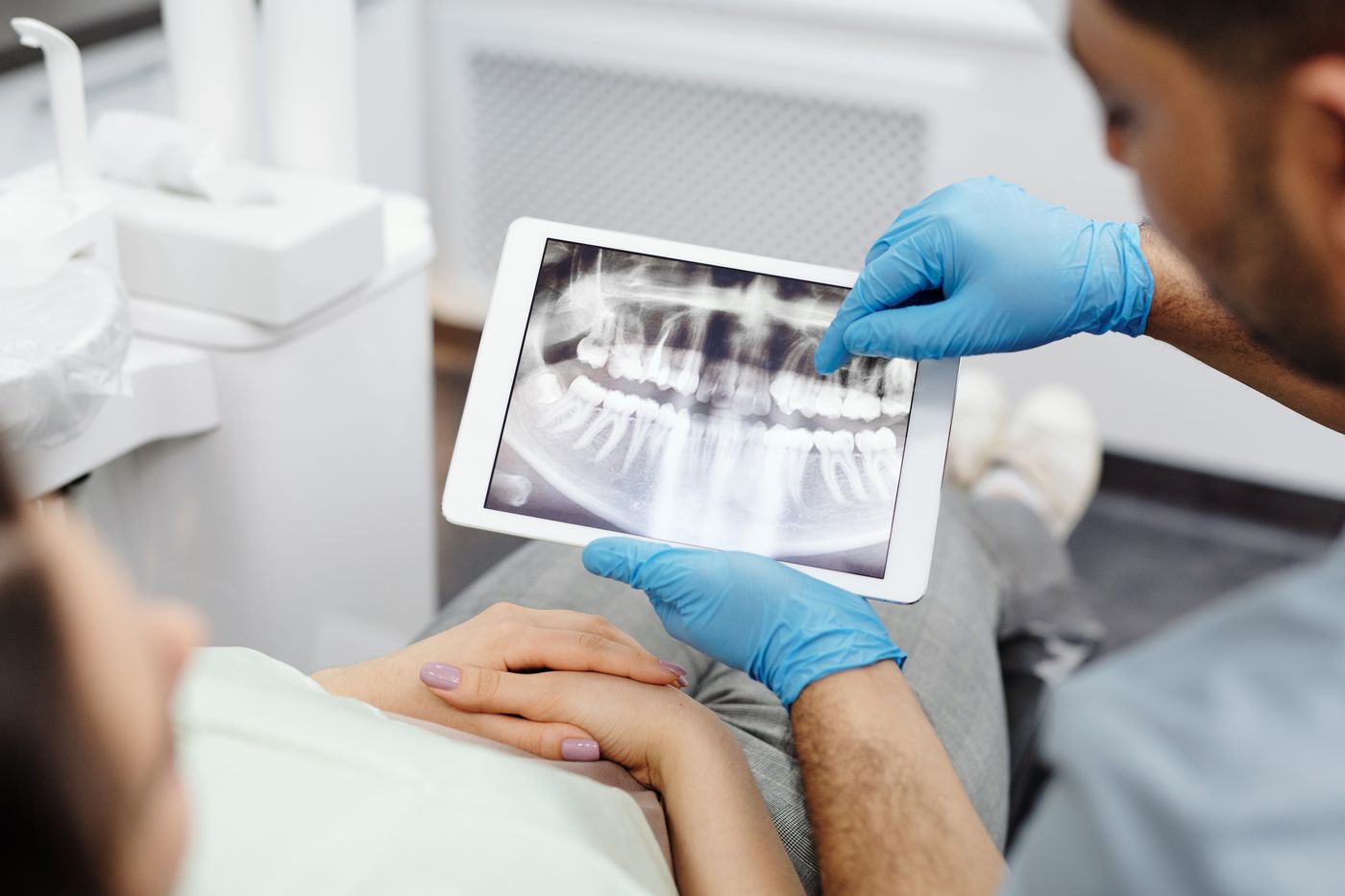 A dentist points to a dental X-ray on a tablet while a patient listens